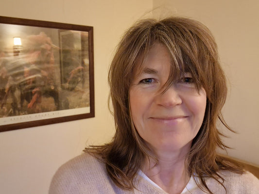 Headshot of Jo smiling at the camera. Framed picture on wall in background. Jo is wearing a pale pink jumper.