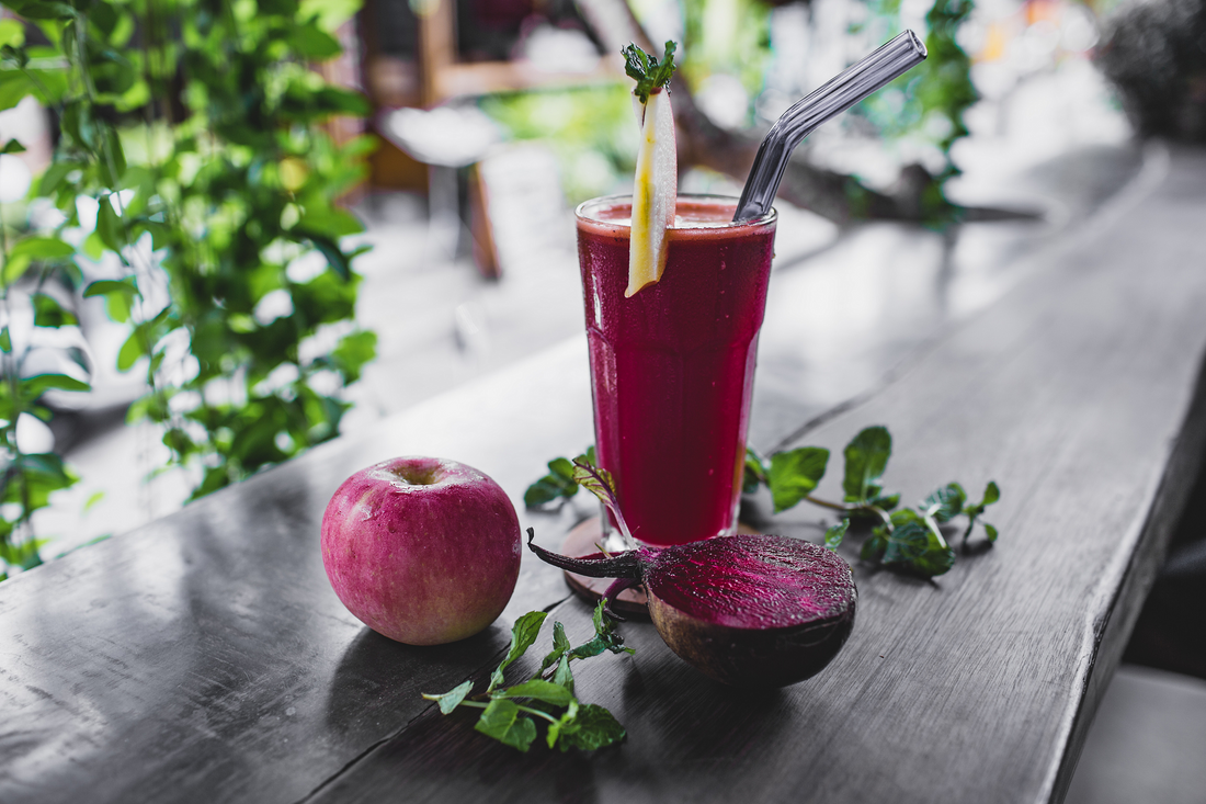 A beetroot and apple smoothie on a dark wood table with an apple and half a beetroot in the foreground