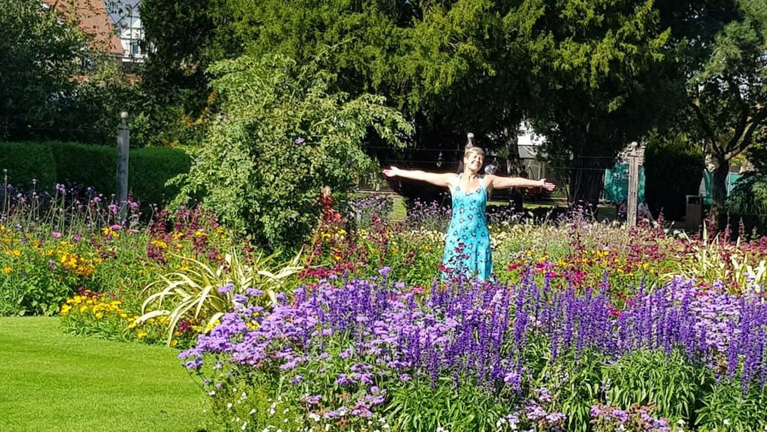 a woman having fun standing in the middle of a colourful flower bed with arms outstretched