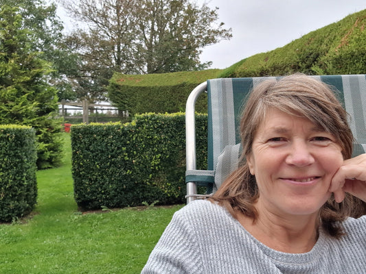 Jo smiling at camera in foreground with green garden, hedges and trees in background