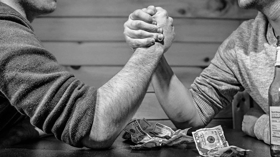 two men arm wrestling with elbows on wooden table and money lying between them