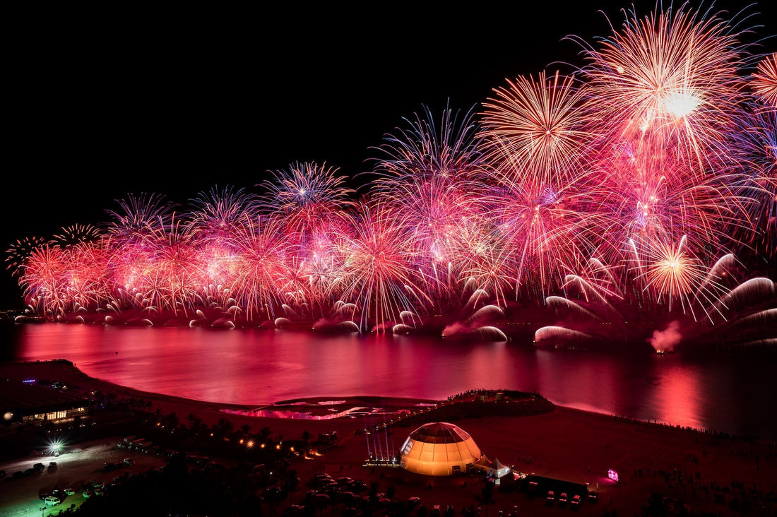a row of pink and gold fireworks along the edge of a river against a dark night sky