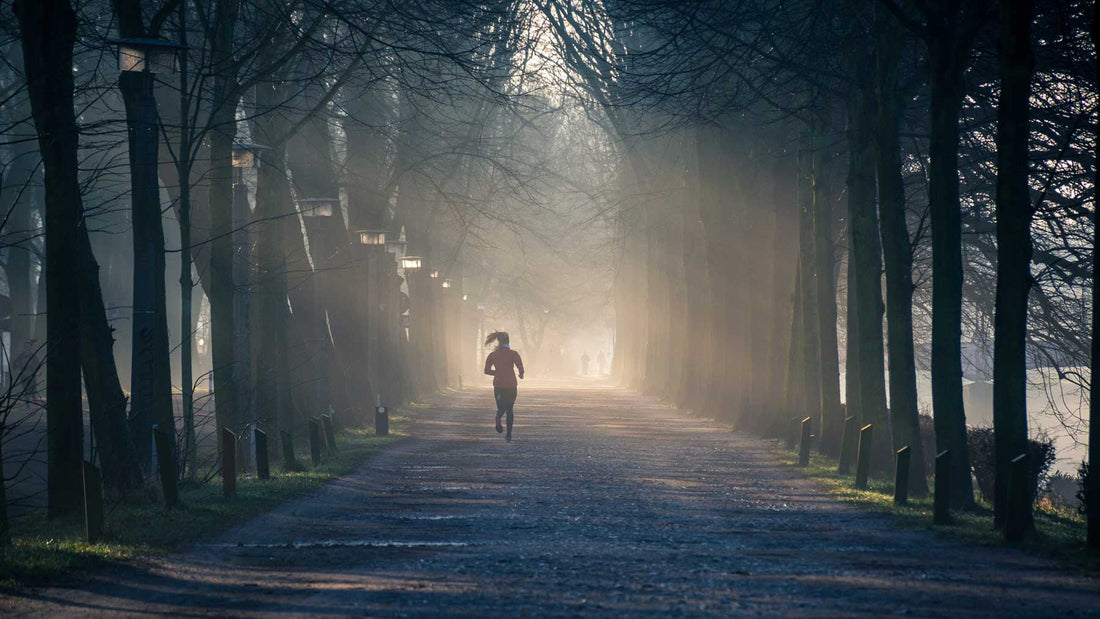 woman running through avenue of trees with sunlight filtering through