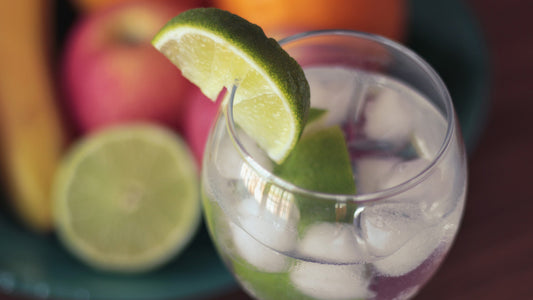 aerial view of glass of water with ice and slice of lime and fruit on table in background