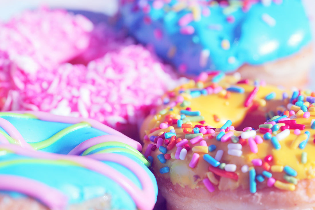 four colourful iced doughnuts in pinks, blues, yellows with multi-coloured hundreds and thousands