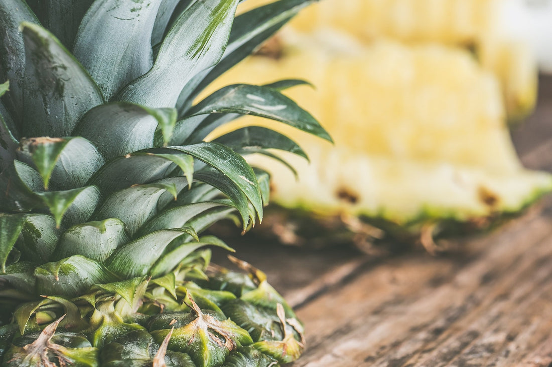 close up of whole pineapple in foreground and slices of pineapple in background on wooden surface