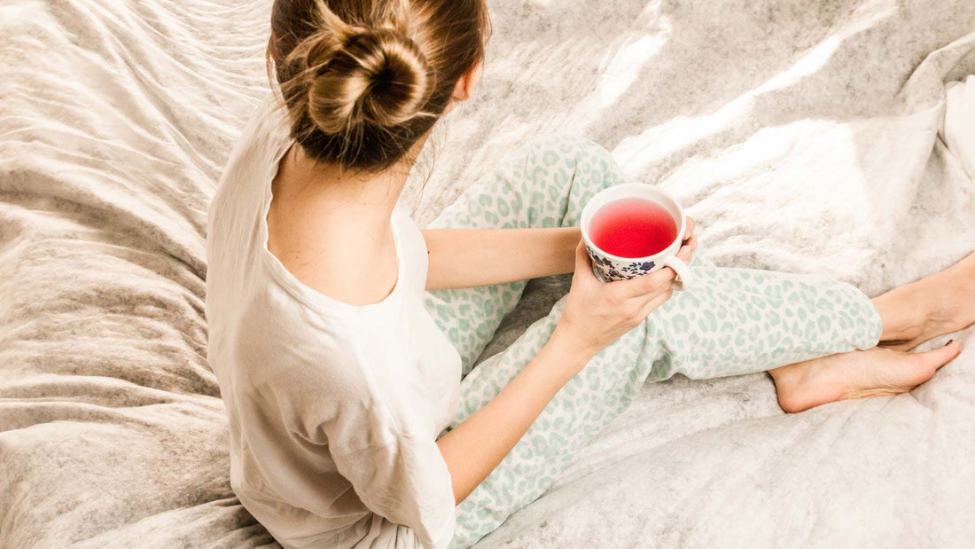 a woman relaxing on a duvet with cup of herbal tea to represent feeling good at the end of a sober day
